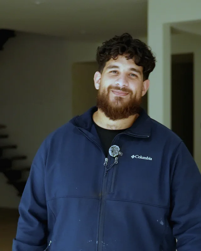 The owner of H&S Plumbing in a navy jacket, smiling in the living room of a new Houston home.